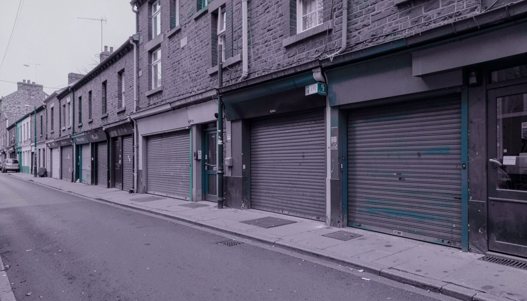 Duotone slate-purple and teal photograph of a row of closed shopfronts on a quiet street, soft grey light, small-business atmosphere